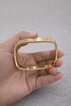Anti-Tarnish, Ashaarya, Ashaarya Jewels, Ashaarya Jewellery, Gold bracelet held in a hand against a gray background