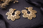 Gold floral earrings on a dark textured surface with dried flowers and black ribbons.
Color: Gold