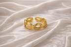 Anti-tarnish gold adjustable twist ring with infinity rope design, open back for flexible sizing, displayed on hand against satin background — lightweight comfort jewellery by Ashaarya. Gold bracelet on a textured beige fabric background