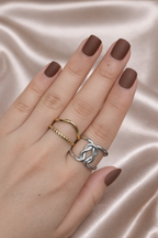 Anti-tarnish gold and silver duo ring stack worn on hand — adjustable comfort jewellery featuring twisted band and knot design, band rings for women, statement rings for women. Hand with brown nail polish wearing two rings on a satin background