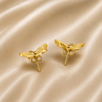 A pair of gold dragonfly stud earrings displayed on a draped beige satin fabric background. anti tarnish earrings, comfort jewellery, butterfly earrings, butterfly stud earrings, gold butterfly earrings, stud earrings for women, lightweight earrings, everyday earrings, stainless steel earrings, hypoallergenic earrings, skin friendly earrings, nature inspired jewellery, minimal earrings, dainty gold earrings, cute earrings for women, butterfly jewellery, anti tarnish jewellery, gold stud earrings, everyday l