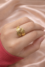 Anti-tarnish gold leaf design ring worn on hand, featuring textured wrap detailing, photographed against champagne satin background — comfort jewellery by Ashaarya. Gold ring on a person's finger against a pink fabric background
