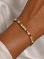 A gold-toned evil eye charm bracelet with clear rhinestones, shown worn on a person's wrist against a soft white fabric background.